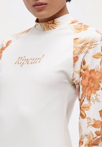 Bijela dugorukava majica s uzorkom cvijeća u narančastoj i žutoj boji na rukavima. "Ripcurl" logo u usklađenoj boji preko prsa.