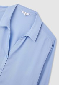 Jasnoniebieska koszula z guzikami, z kołnierzykiem, wykonana z gładkiego materiału, charakteryzująca się luźnym krojem i minimalistycznymi detalami.