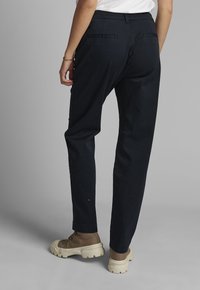Pantalon bleu marine en coton, doté d'une coupe droite, de deux poches arrière et d'une ceinture standard. Associé à des bottes marron.