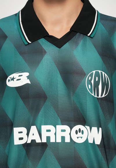 Maillot en jersey à motifs géométriques verts et noirs, avec un col noir et des logos blancs, arborant le texte "BARROW" et un détail de conception graphique.