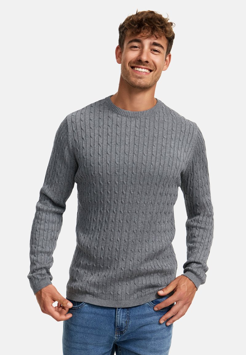 Grå kabelstrikket genser med rund hals og ribbede mansjetter, kombinert med blå jeans. Har et teksturert mønster gjennom hele.