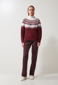 Bordeaux gebreide trui met witte geometrische patronen, hoge ribgebreide kraag, gecombineerd met bordeaux corduroy broek en witte sneakers.