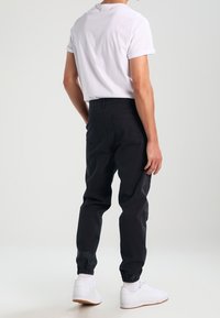 Black jogger pants with elastic cuffs, made of cotton blend. Worn with a white short-sleeve t-shirt and white sneakers.