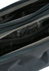Bolsa de tela azul oscura con múltiples compartimentos con cremallera. Superficie texturizada y forro interior gris visible, con un patrón de nombre de marca.
