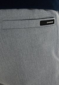 Lichtgrijze broek met een gladde textuur, voorzien van een achterzak en een zwart merklabel. Eenvoudig, modern ontwerp zonder patronen.