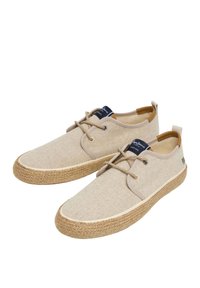 Scarpe di tela beige con suole in juta intrecciata, punta tonda, design con lacci e dettagli marroni sul tallone e sulla linguetta. Etichetta del marchio nera visibile.