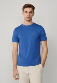 Niebieska bawełniana koszulka z okrągłym dekoltem i krótkimi rękawami. Posiada kieszeń z haftowanym wykończeniem po lewej stronie klatki piersiowej.