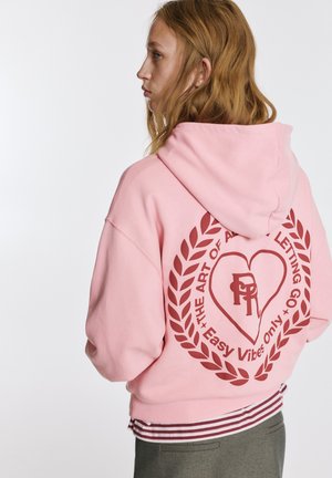 Rózsaszín kapucnis pulóver nagy nyomtatott grafikával a hátoldalán, szöveggel és szív díszítéssel. Puha, texturált anyag bordázott mandzsettákkal.