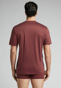 Bordo krótki T-shirt z gładką teksturą i okrągłym dekoltem, połączony z pasującymi szortami. Widok z tyłu ukazuje subtelne boczne rozcięcia.