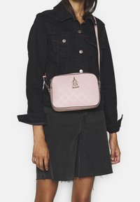 Rosa Umhängetasche aus strukturiertem Material, mit einem Verschluss mit einem "G"-Logo, kontrastiert mit einer schwarzen Jeansjacke und einem Rock.