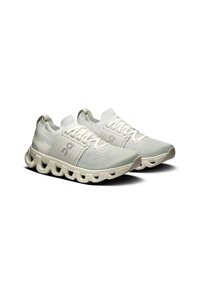 Baskets de sport gris clair avec une tige en tricot respirant, des accents texturés et une semelle distinctive et rembourrée avec un design en forme de vague.