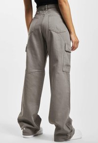 Pantalons cargo gris en coton, présentant des jambes larges, des poches latérales et une coupe décontractée ; tissu texturé avec des détails de couture visibles.