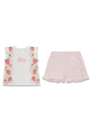 Haut blanc sans manches avec imprimé fraises et fleurs et texte rose « Guess Fruit party », associé à un short à rayures rose clair avec volants.