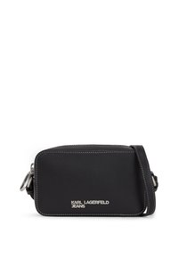 Sac bandoulière en faux cuir noir avec des coutures blanches et des éléments en métal argenté. Présente le logo de la marque à l'avant et une bandoulière réglable.