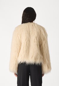 Chaqueta de pelo sintético en blanco roto con una apariencia texturizada y peluda. Presenta un corte relajado y mangas anchas, con un dobladillo corto.