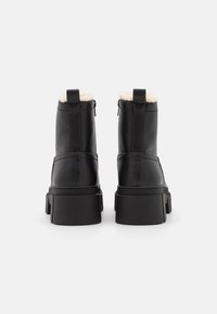 Bottines en cuir noir avec une finition texturée, doublure en fausse fourrure et semelle épaisse noire. Comprend une fermeture éclair à l'arrière.