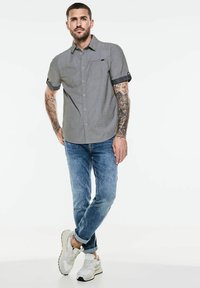 Kortärmad grå skjorta med knappar och bröstficka, samt kontrasterande marinblå manschetter. Kombinerad med blå jeans och vita sneakers.