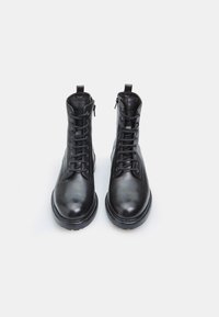 Stivali neri in pelle fino alla caviglia con una texture liscia, design con lacci e chiusura laterale con zip. Presentano una suola in gomma e una forma della punta arrotondata.