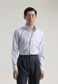 Camisa de cuadros azul claro con botones y cuello estructurado, combinada con pantalones de vestir oscuros con pliegues. Tejido de algodón suave, ajuste a medida.