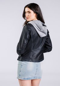 Schwarze Lederjacke mit grauem Kapuzen, mit taillierter Passform und detaillierter Nahtführung. Kombiniert mit einem hellen Denim-Minirock.