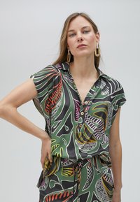 Satin short-sleeve shirt with a leafy pattern in green, black, orange, and pink, featuring a collar and button detail at the front.