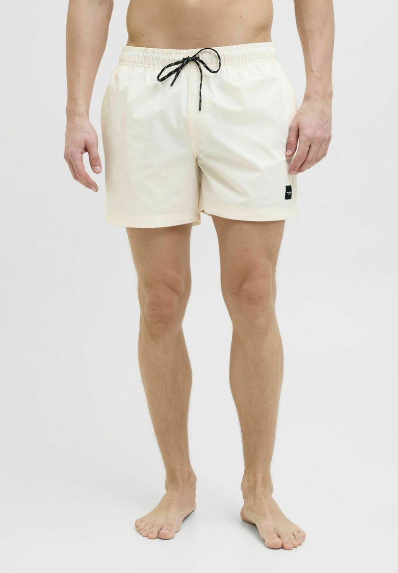 Costumi da bagno da uomo, color crema chiaro, con vita elasticizzata e laccio nero, tasche laterali e piccolo logo sul lato sinistro.