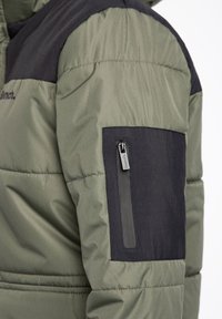 Manche de veste matelassée verte et noire avec une poche zippée noire et un curseur de fermeture éclair marqué "Bench" visible.