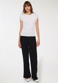 Biała bluzka z krótkim rękawem w kropeczki z srebrnymi zdobieniami, w połączeniu z czarnymi spodniami o szerokich nogawkach oraz czarno-białymi butami.