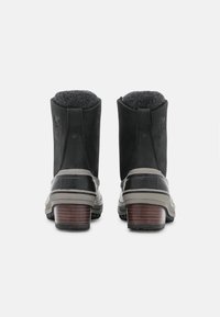 Botas de ante negras hasta el tobillo con una base de goma gris y tacón de madera. Forro de fieltro en el collar. Presenta el logotipo en el lado exterior.
