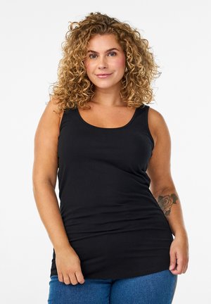 Mujer con cabello rizado que lleva una blusa negra sin mangas y jeans azules, mostrando un tatuaje de una rosa en su antebrazo izquierdo.