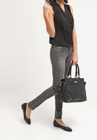 Blusa negra sin mangas, jeans slim grises, bailarinas negras y un bolso negro estructurado con diseño acolchado y tachuelas plateadas.