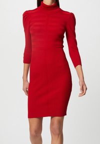 Rotes geripptes Strickkleid mit hohem Hals, figurbetontem Schnitt und drei Viertelärmeln; es hat eine gestreifte Textur und weichen Stoff.