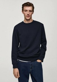 Felpa blu navy in tessuto misto cotone, con scollo rotondo, polsini e orlo a coste, abbinata a jeans blu scuro, texture liscia, vestibilità casual.