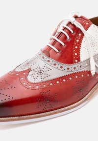 Καφέ και λευκό δερμάτινο παπούτσι brogue με διακοσμητικές τρύπες και λευκά κορδόνια σε φωτεινό φόντο.