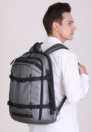 Gray backpack with black straps, multiple compartments, and an orange accent. Made of durable material, featuring a sleek, rectangular design.
