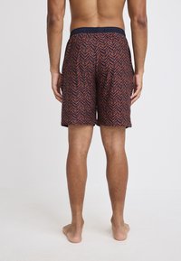 Zwemshorts voor mannen met een rood en marineblauw chevron patroon. Elastische tailleband en knielengte, gemaakt van lichte, gestructureerde stof.