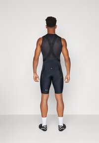Menns sykkelbukseshorts i mørk marineblått stoff. Har kryssryggstropper, polstret seteområde og minimale reflekterende detaljer for synlighet.