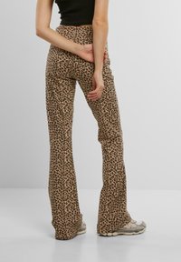 Kalhoty s flérovým střihem v leopardím vzoru v béžové a hnědé barvě, s vysokým pasem a hladkým povrchem, v kombinaci se šedými teniskami.