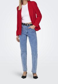 Rød tekstureret blazer, hvid cropped t-shirt, højtaljede lyseblå jeans, sort bælte og sorte flade sko. Minimale accessories og enkel pasform.