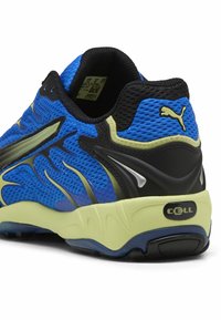 Chaussure de sport en maille bleue avec des accents noirs, semelle vert citron, surface texturée et détails argentés. Équipée d'un col rembourré et d'un logo.
