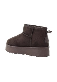 Brązowy zamszowy botek za kostkę o miękkiej fakturze, z okrągłym noskiem, lekko podniesioną gumową podeszwą i pętelką z tyłu. Minimalne detale przeszyć.