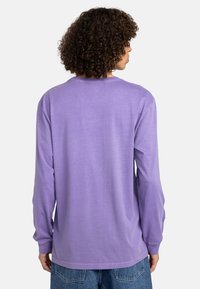 Langärmliges lila T-Shirt aus weicher Baumwolle, mit Rundhalsausschnitt und lockerer Passform. Die Rückansicht zeigt ein minimalistisches Design.