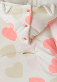 Valkoinen kangas, jossa on suuria pastelliväreissä sydämiä vaaleanpunaisena, korallina ja beigeä; sisältää röyhelökauluksen ja oranssit nepparit; mukana horisontaalinen avaus.