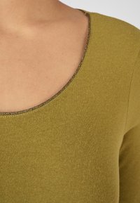 Suéter verde oliva con escote en forma de barco, que presenta un borde dorado brillante a lo largo del cuello. Textura suave y diseño ajustado.