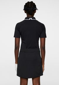 Svart golfoutfit som består av en kortärmad polo och en matchande kjol. Skjortan har en vit krage och diskret logotyp på midjebandet.