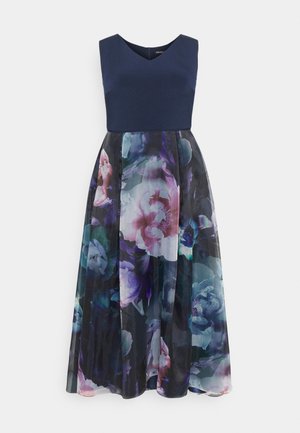 Ærmeløs marineblå topkjole med en blomstretrykt A-line nederdel i nuancer af lilla, pink og teal på en sort baggrund.