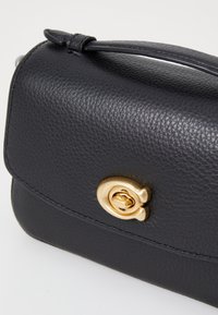 Schwarze Lederhandtasche mit strukturierter Oberfläche, ausgestattet mit einem goldfarbigen Verschluss und einem schmalen Griff. Kompakte rechteckige Form, klare Linien.