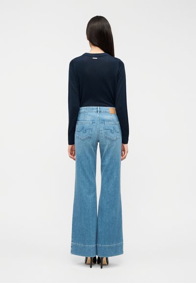 Μπλε ναυτικό πουκάμισο με μακριά μανίκια σε συνδυασμό με ανοιχτό μπλε παντελόνι φαρδύ πόδι που διαθέτει πίσω τσέπες και καφέ δερμάτινο έμπλαστρο στη μέση.