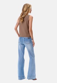Bruine mouwloze top met een gestructureerde achterkant, gecombineerd met lichtblauwe flare jeans met een zak en randdetails.