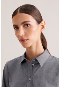 Camicia grigia con colletto, realizzata in tessuto strutturato, con chiusura frontale a bottoni di cui due visibili e colletto strutturato.